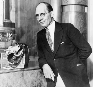 Charles Kettering, ingeniero estadounidense e inventor del motor de arranque eléctrico para automóviles, posando junto a un modelo mecánico en exhibición.
