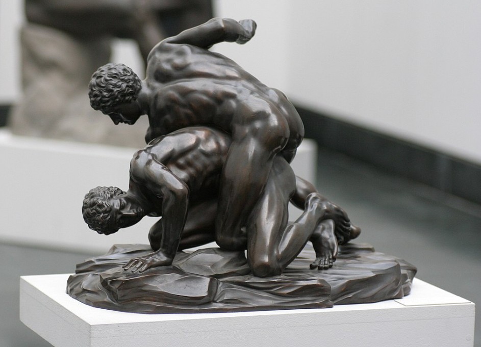 Escultura en bronce que representa una escena de combate de pancracio entre dos luchadores desnudos en el suelo, basada en un modelo griego del siglo III a.C., reproducida en mármol en época romana y esta copia reducida realizada alrededor de 1900, conservada en las Colecciones Estatales de Antigüedades.