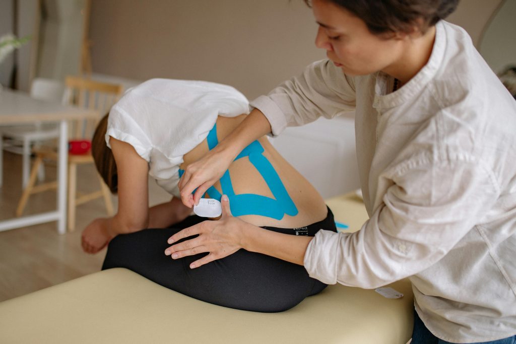 Terapista aplicando cinta kinesiotape en la espalda de una persona, en una sesión de tratamiento físico para aliviar dolores musculares.