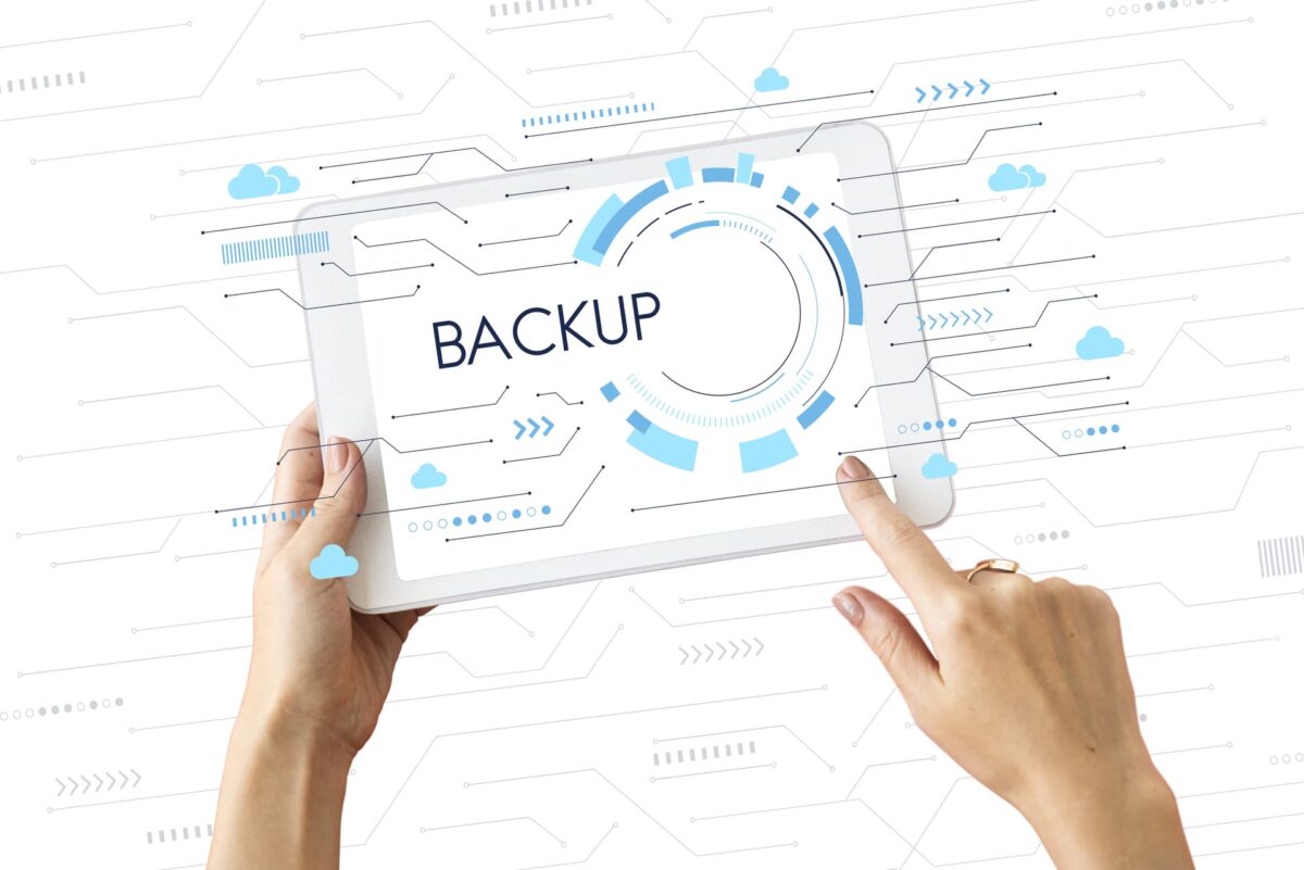 Manos sosteniendo una tablet con la palabra “Backup” en pantalla y gráficos digitales sobre un fondo tecnológico con iconos de nube.