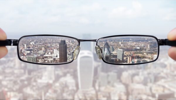 Gafas enfocando un paisaje urbano mientras el fondo aparece borroso, representación de problemas de visión y corrección visual.