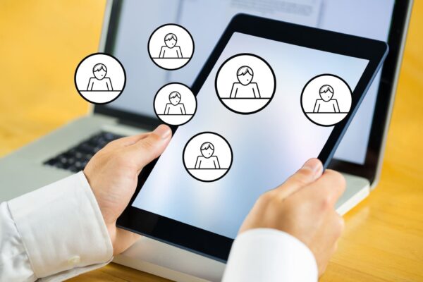 Manos sosteniendo una tablet con iconos de usuarios en pantalla, representando gestión de clientes o red de contactos digital.