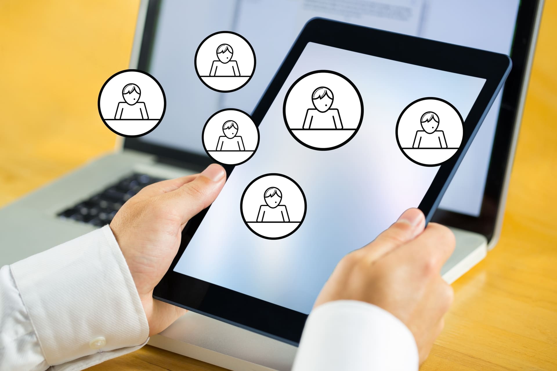 Manos sosteniendo una tablet con iconos de usuarios en pantalla, representando gestión de clientes o red de contactos digital.