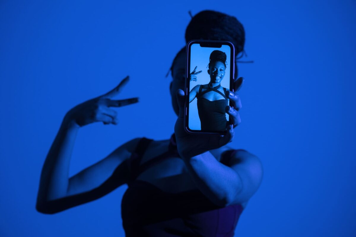 Mujer sosteniendo un smartphone frente a la cámara en un entorno iluminado con luz azul, mostrando una imagen en la pantalla.