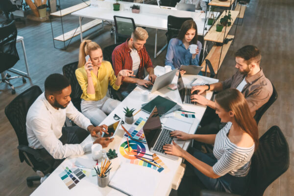 Equipo colaborando alrededor de una mesa con ordenadores portátiles, una tableta y muestras de color en una oficina